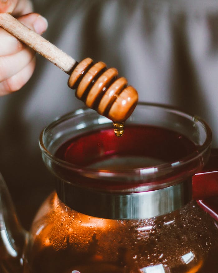 A honey dipper drizzling honey over a steaming coffee carafe in a cozy setting.